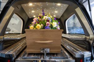 Uitvaartkist met bloemstuk in rouwauto tijdens uitvaart