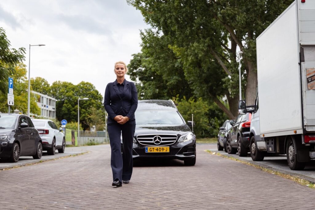 Uitvaartbegeleider loopt voor rouwauto tijdens uitvaart