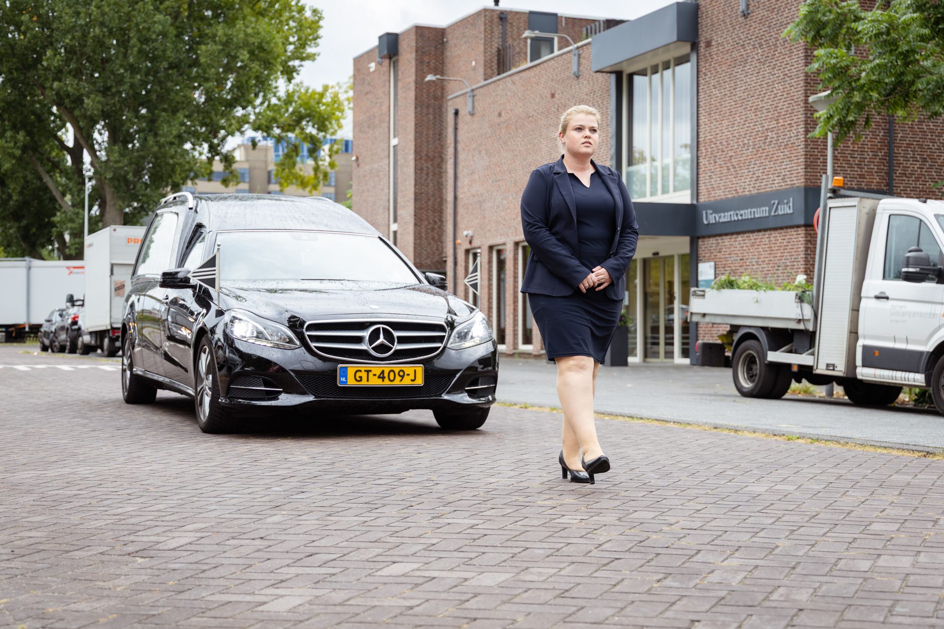 Uitvaartbegeleider loopt voor rouwauto bij uitvaartcentrum