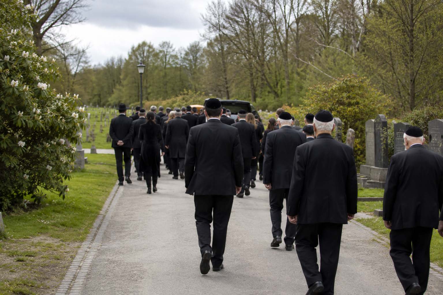 Joodse uitvaart in zaandam: een man met een keppeltje knielt bij een grafsteen op een begraafplaats en legt een steentje neer als teken van respect en herinnering.