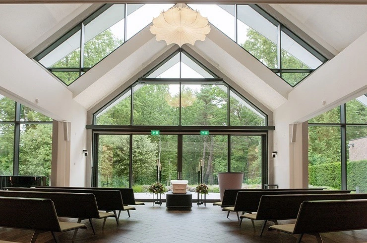 Lichte aula van Crematorium Laren met glazen gevel en uitzicht op bos