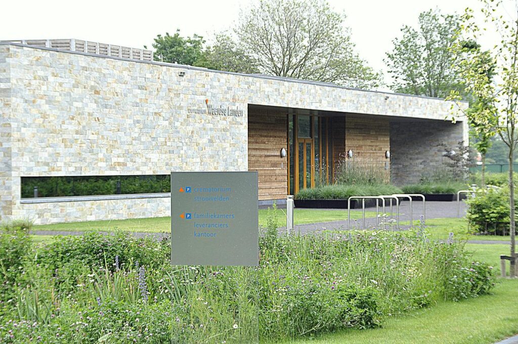 Moderne gevel van Crematorium Waerdse Landen in Heerhugowaard, omgeven door groen met een informatiebord op de voorgrond.