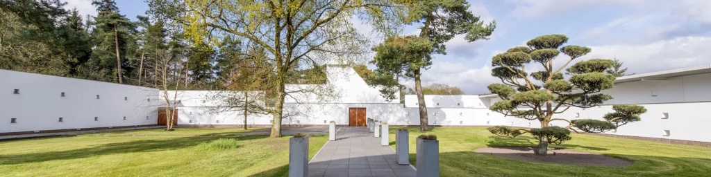 Ingang van het crematorium met wit gebouw, tuinpad en Japanse tuinboom op het terrein