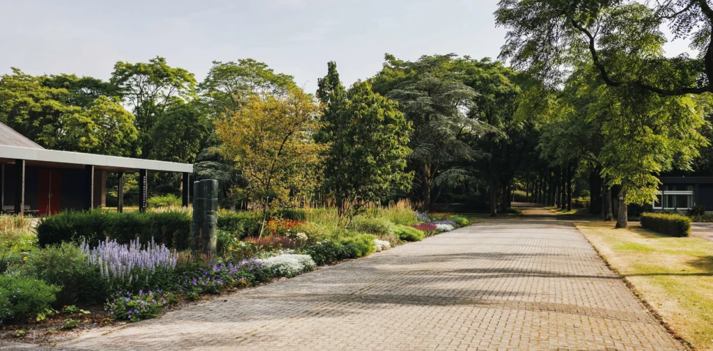Toegangspad naar crematorium Daelwijck in Utrecht, omzoomd door bomen en bloeiende border
