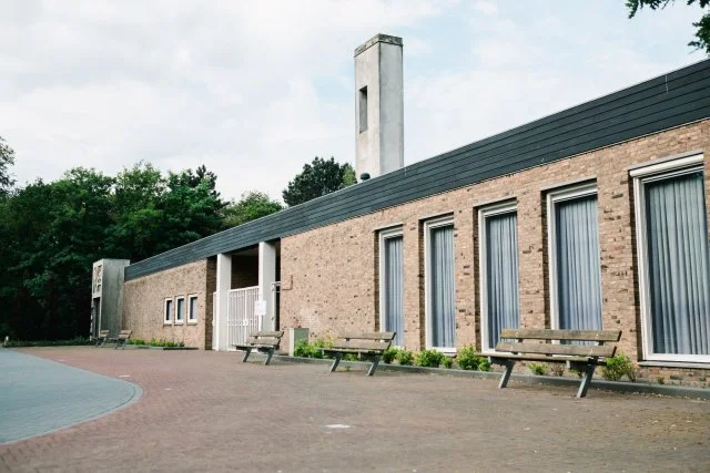 Aulagebouw van begraafplaats Duinrust in Beverwijk, bakstenen gevel met bankjes op het plein